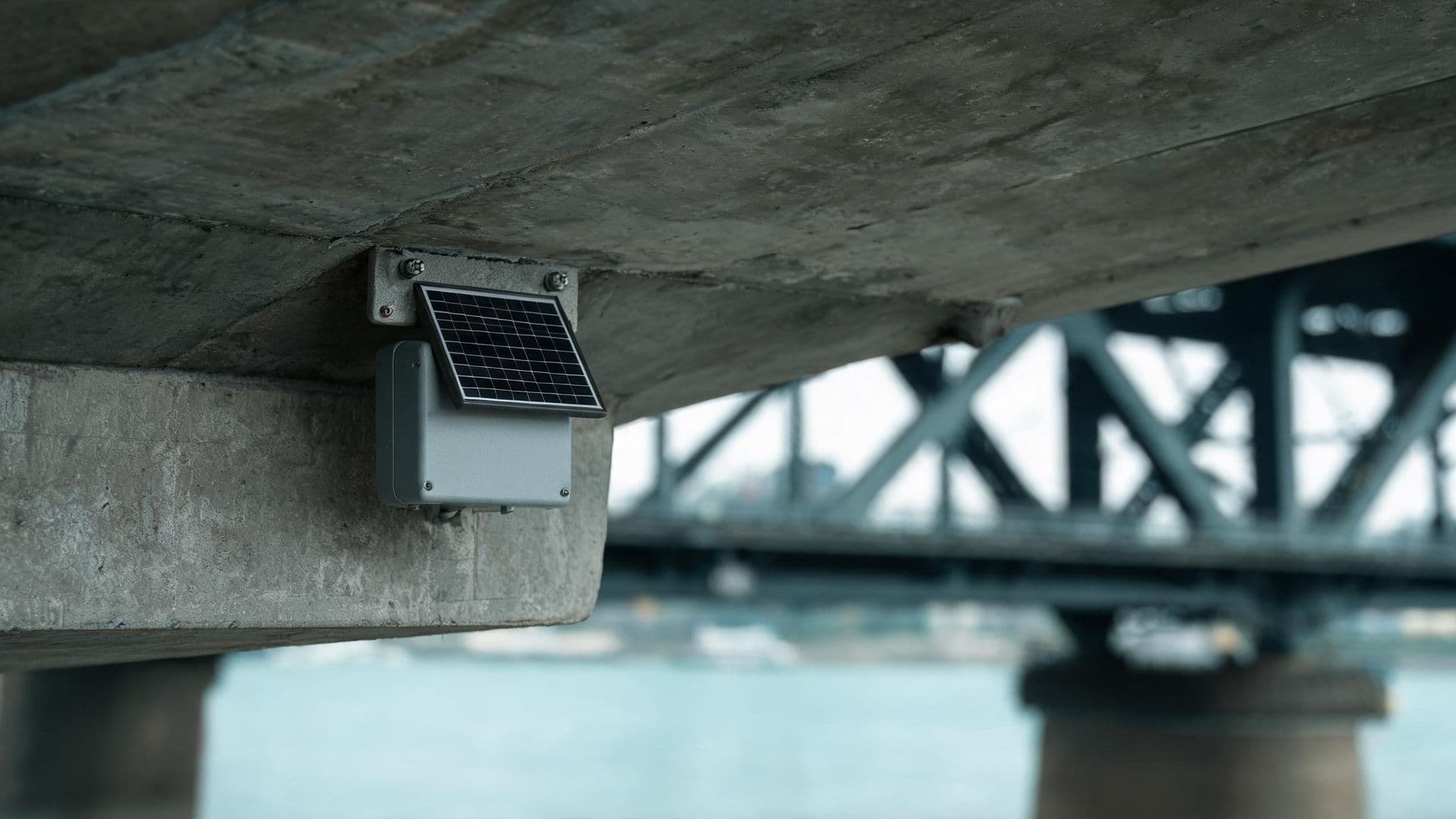 Illustrative photo: a solar-powered sensor module mounted under a highway bridge
